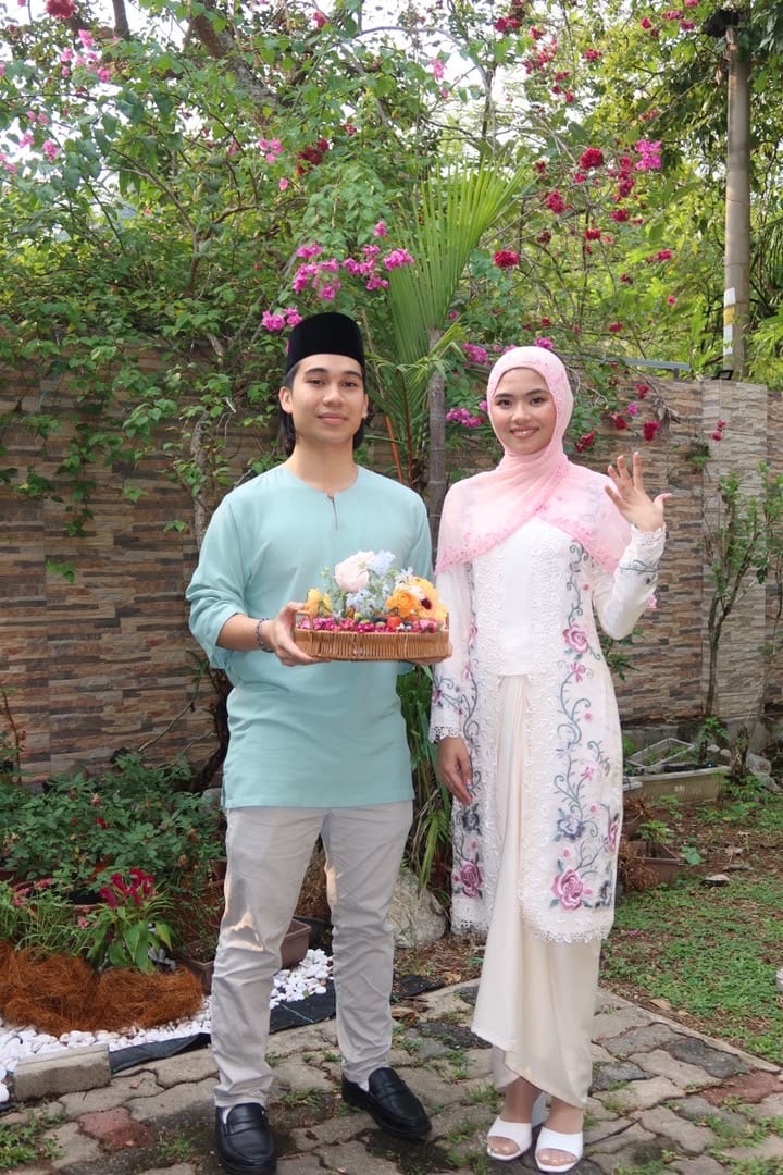 Mia waving beside Arief in the garden